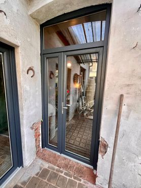 Portes doubles vitrées à cadres gris foncé, encastrées dans une entrée en briques et en pierres patinées.