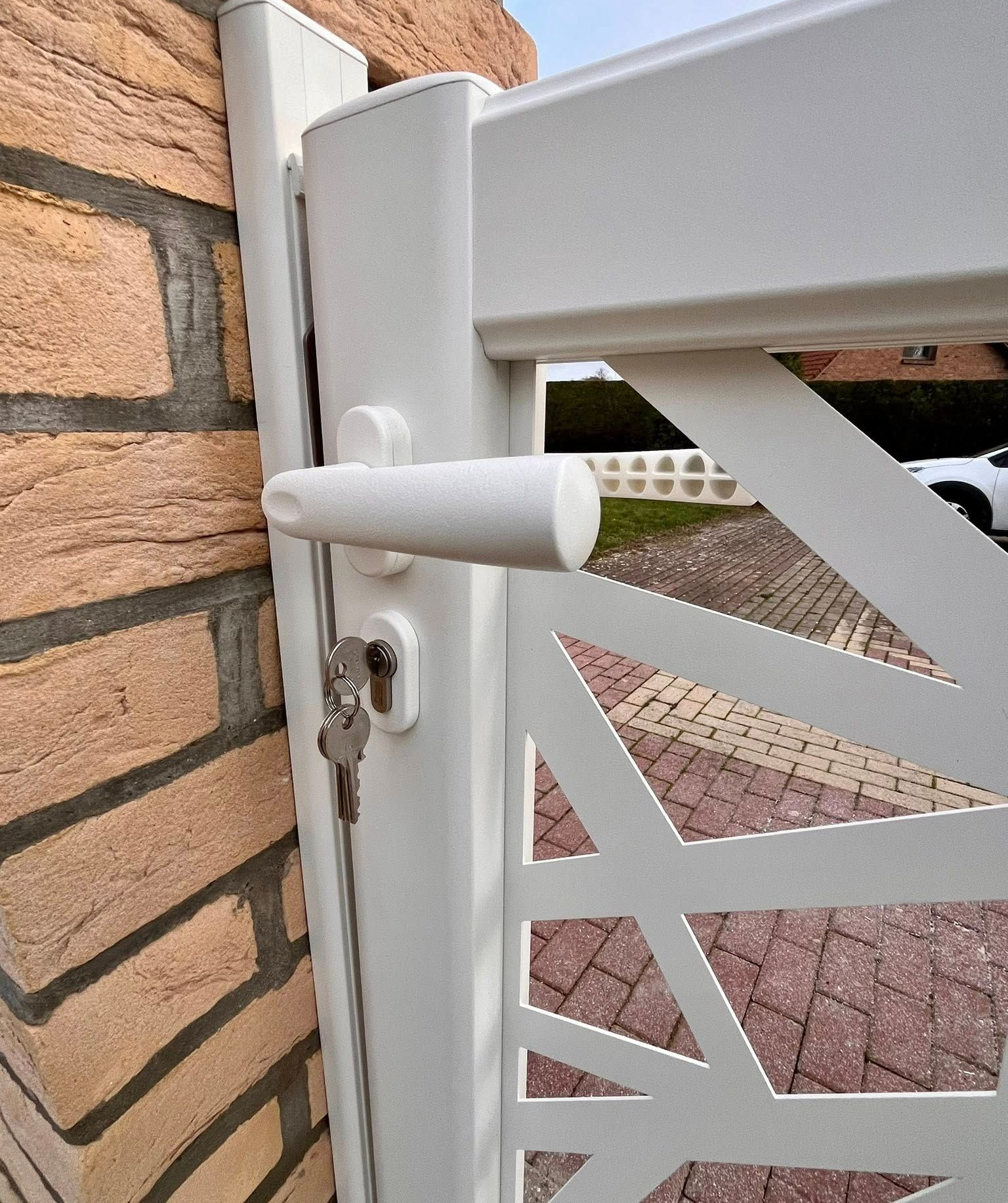Portail blanc avec clé et poignée, fixé sur un mur de briques à motifs.