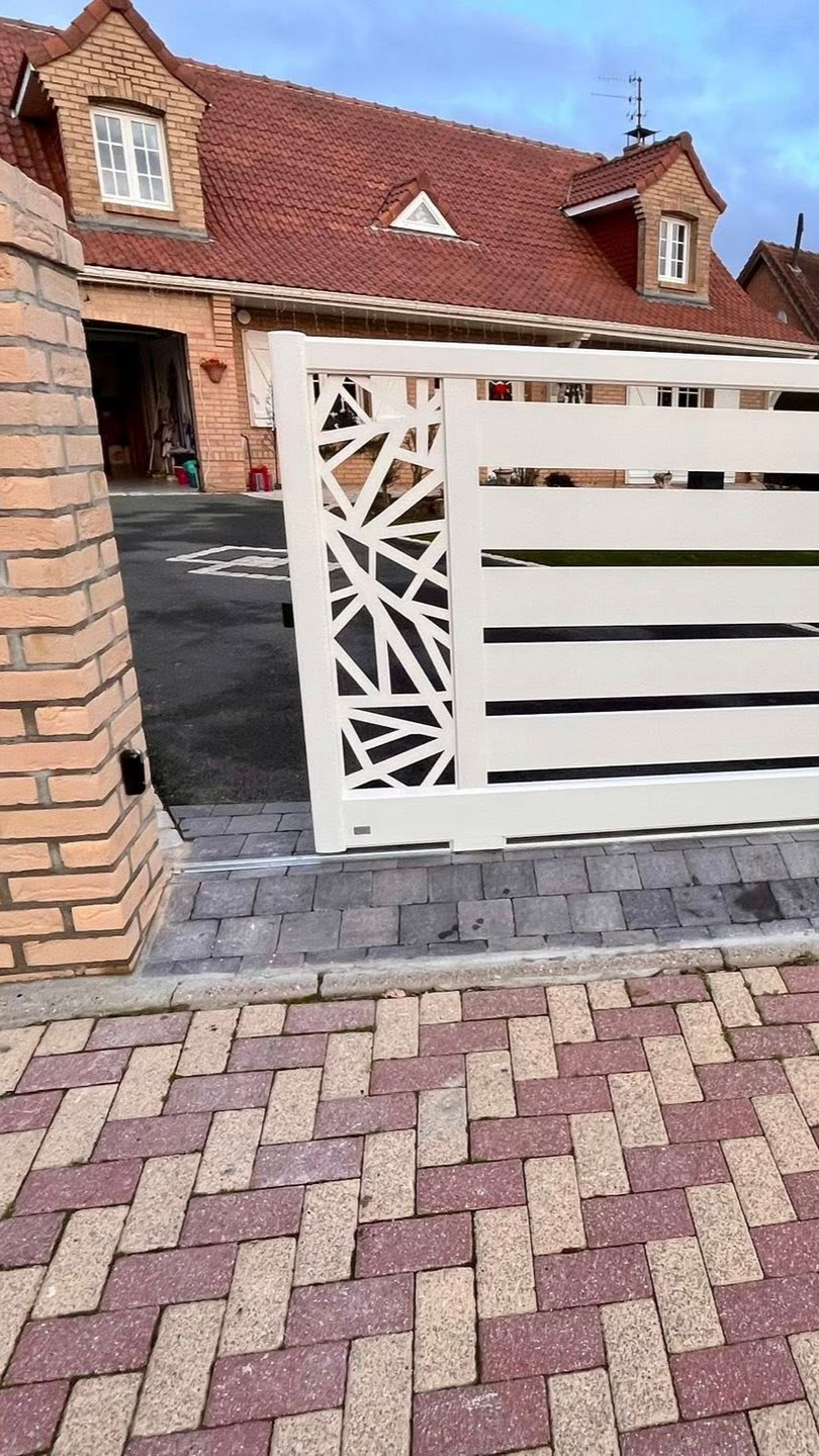 Clôture en métal blanc avec panneau décoratif, maison en briques et allée visibles.