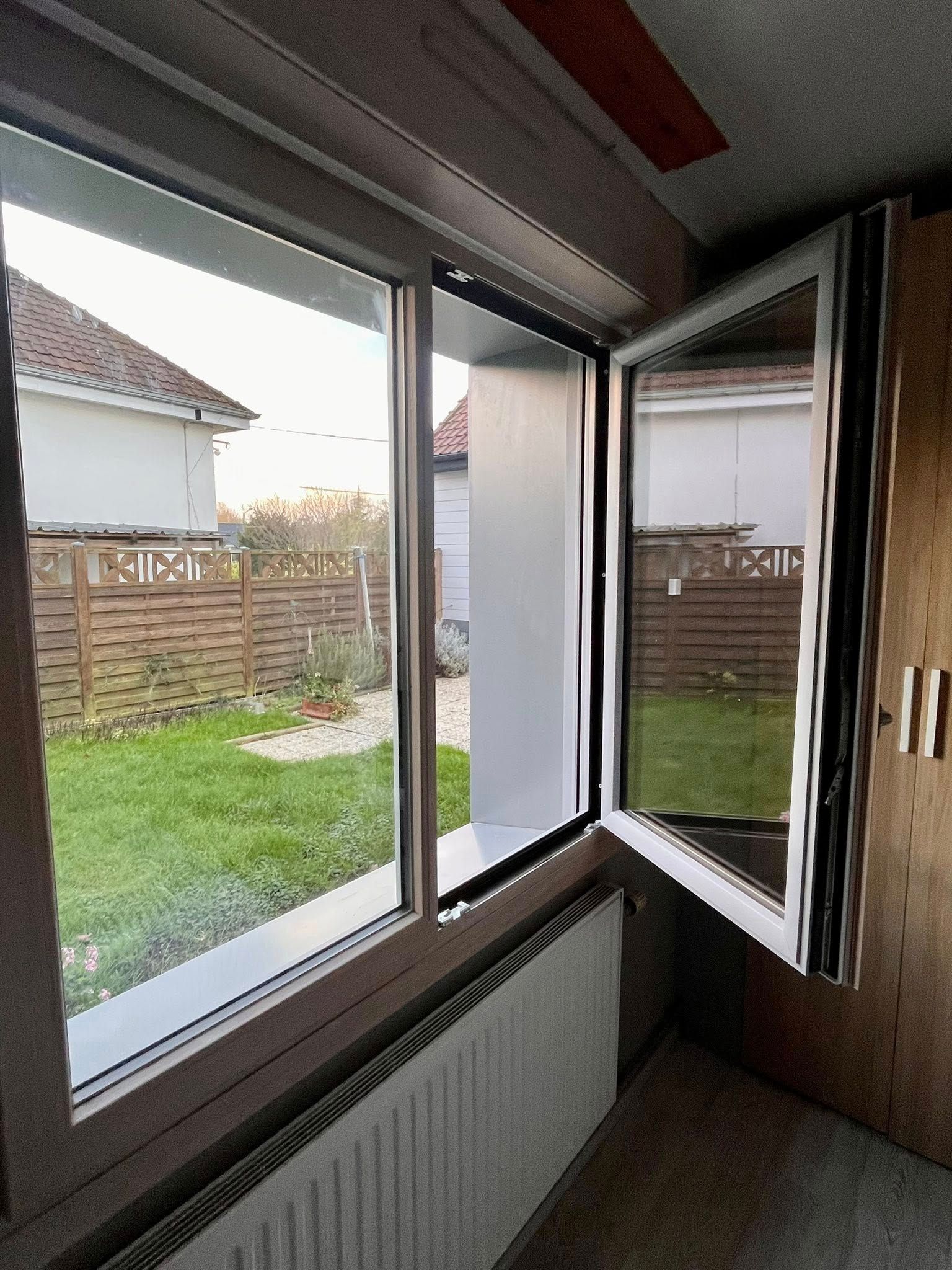 Fenêtre ouverte dans une pièce donnant sur un jardin. Un radiateur se trouve en dessous.