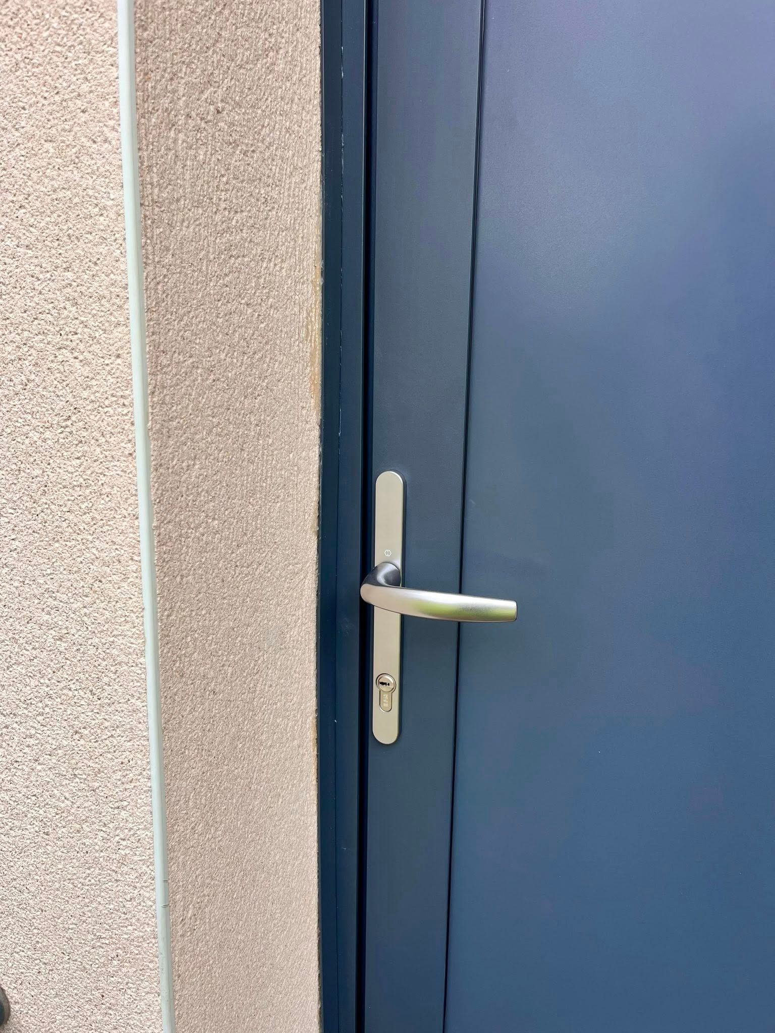 Porte bleue avec poignée et garniture argentées, à côté d'un mur beige texturé.