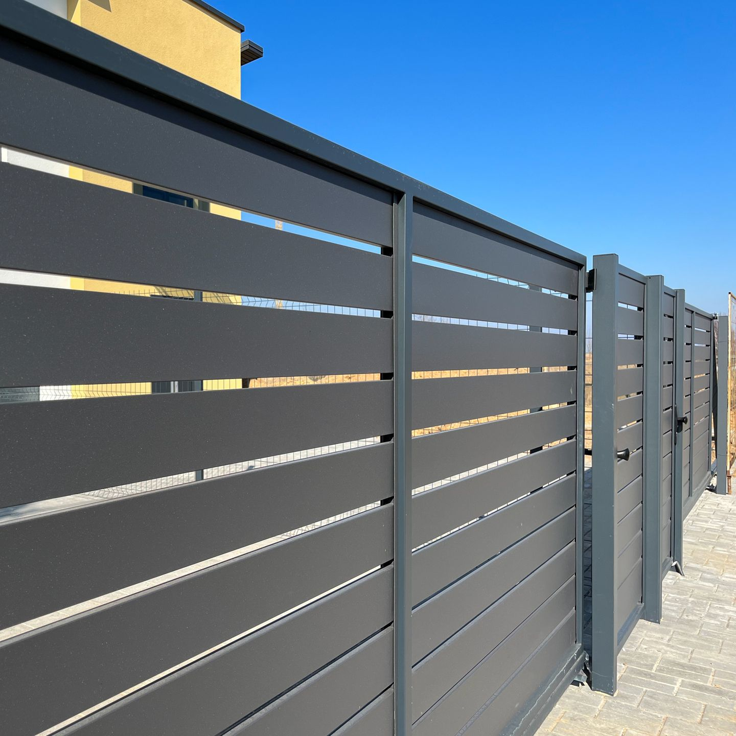 Clôture à lattes horizontales gris foncé avec poteaux, sous un ciel bleu.