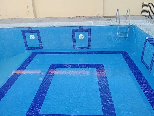 Una gran piscina con azulejos azules y una escalera.