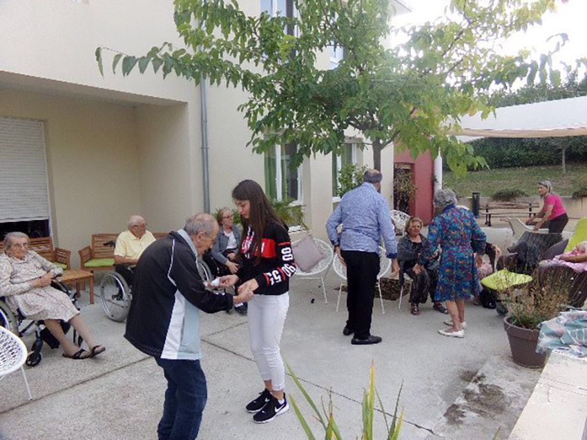 Des personnes dansent en plein air dans un établissement de soins pour personnes âgées, tandis que d'autres sont assises à proximité.