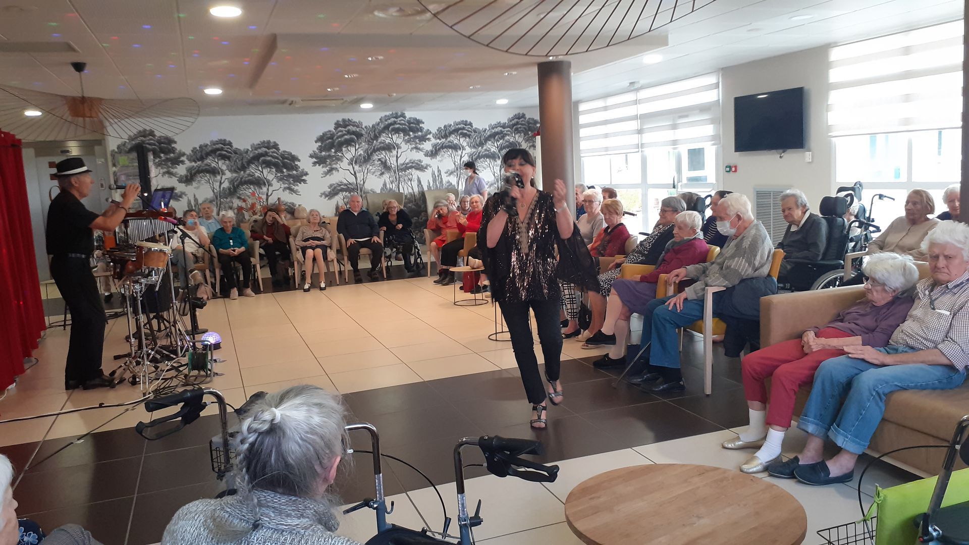 Dans une salle de musique : deux personnes chantent, deux autres jouent de la guitare. Pièce lumineuse avec des œuvres d’art aux murs.