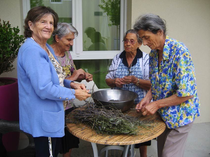 Quatre personnes sont réunies autour d'une table avec des herbes aromatiques. Elles sont à l'extérieur, peut-être en train de jardiner ou de faire du bricolage.