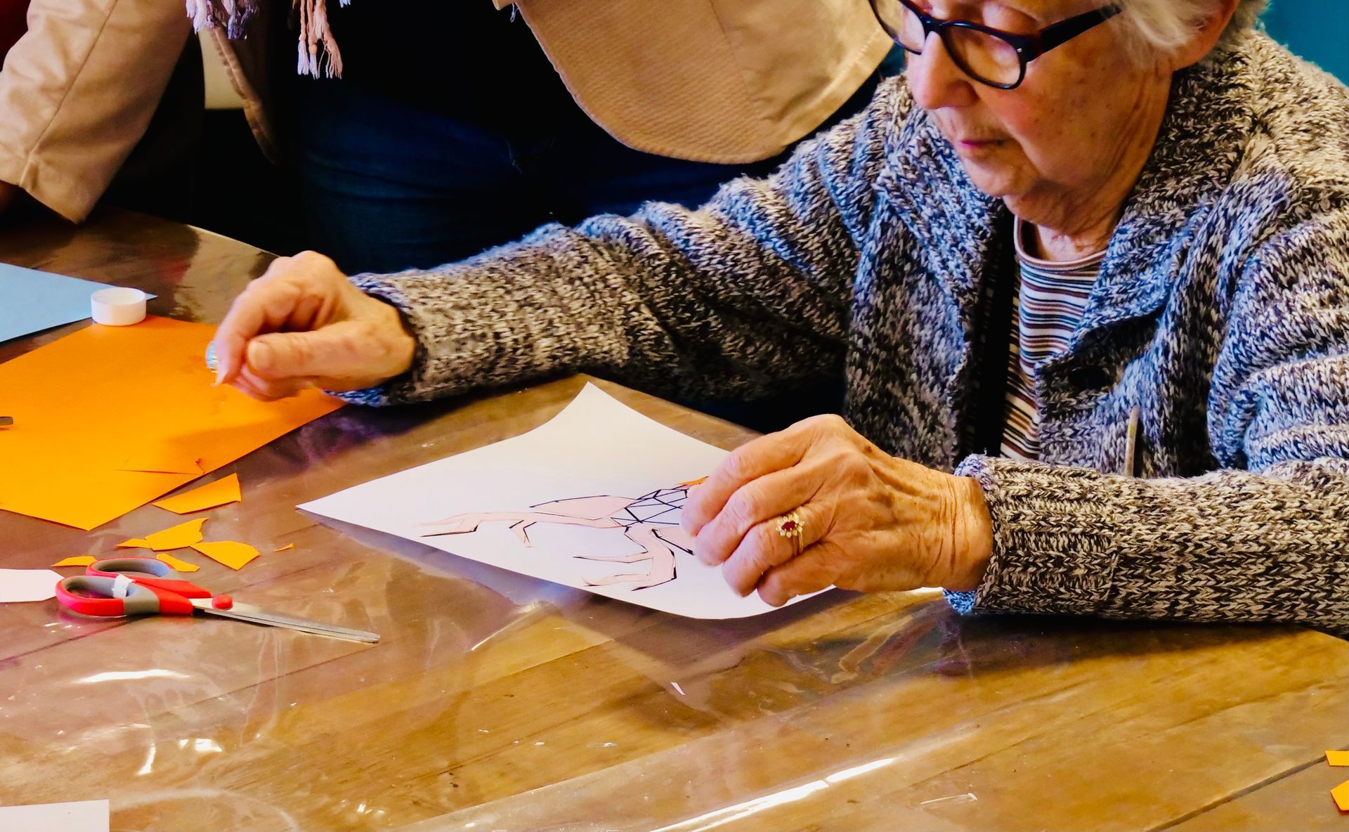 Une personne âgée, portant des lunettes, travaille à un projet de bricolage à une table.