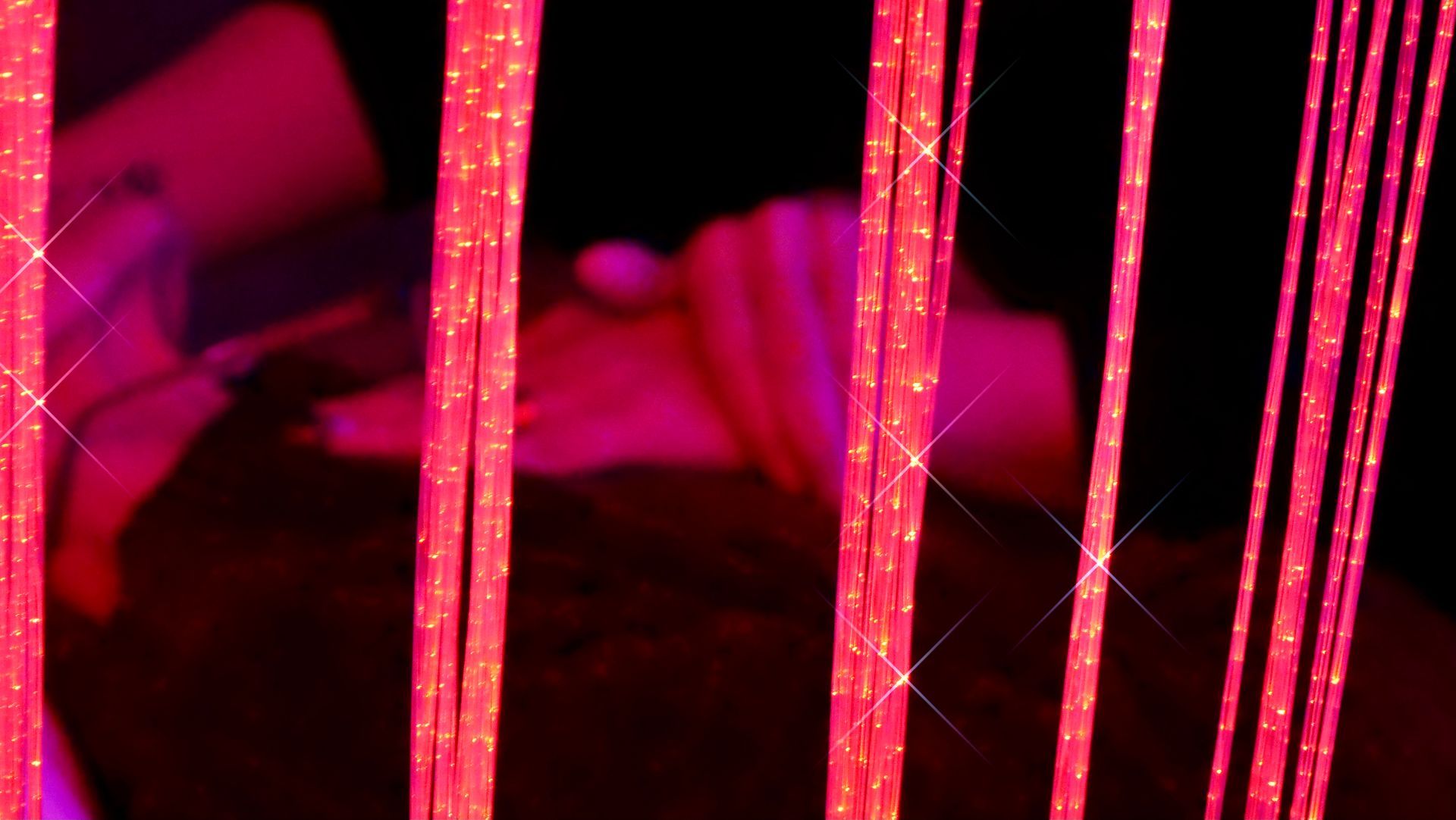 Des mèches roses et scintillantes dissimulent une personne âgée allongée, dans un décor sombre.