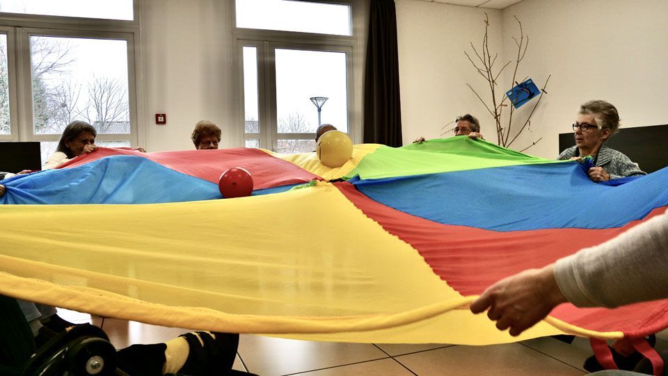 Des personnes jouent à l'intérieur avec un parachute coloré, une balle étant placée au centre.