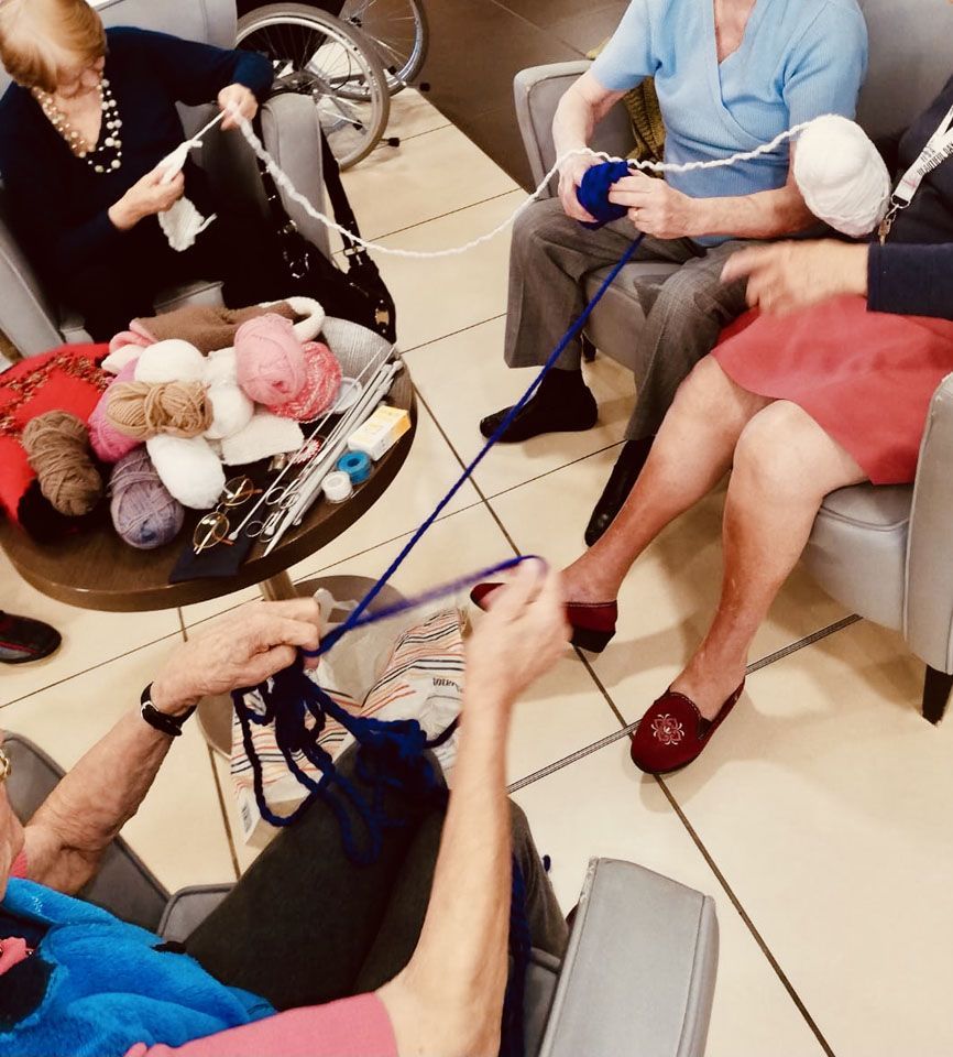 Quatre personnes tricotent ensemble, avec des laines de couleurs différentes, à l'intérieur.