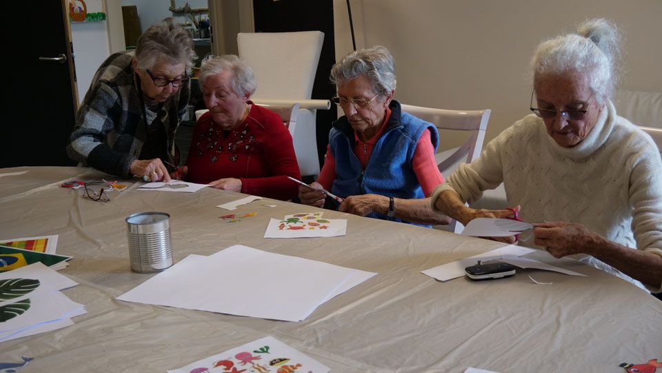 Quatre adultes d'un certain âge sont assis à une table pour bricoler, découpant et assemblant des formes en papier coloré.