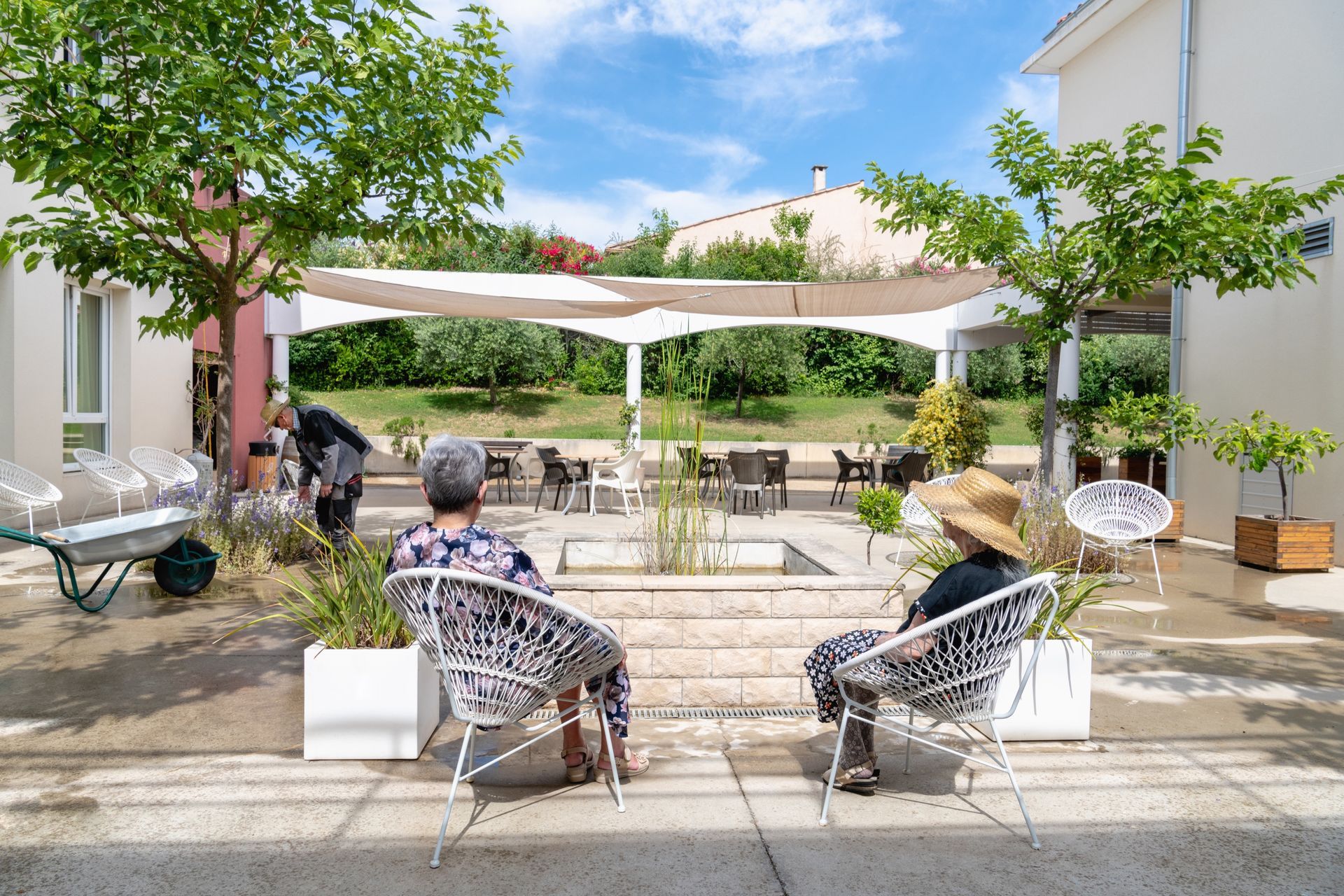 Deux femmes âgées se détendent dans des chaises dans une cour ensoleillée, à l'ombre.
