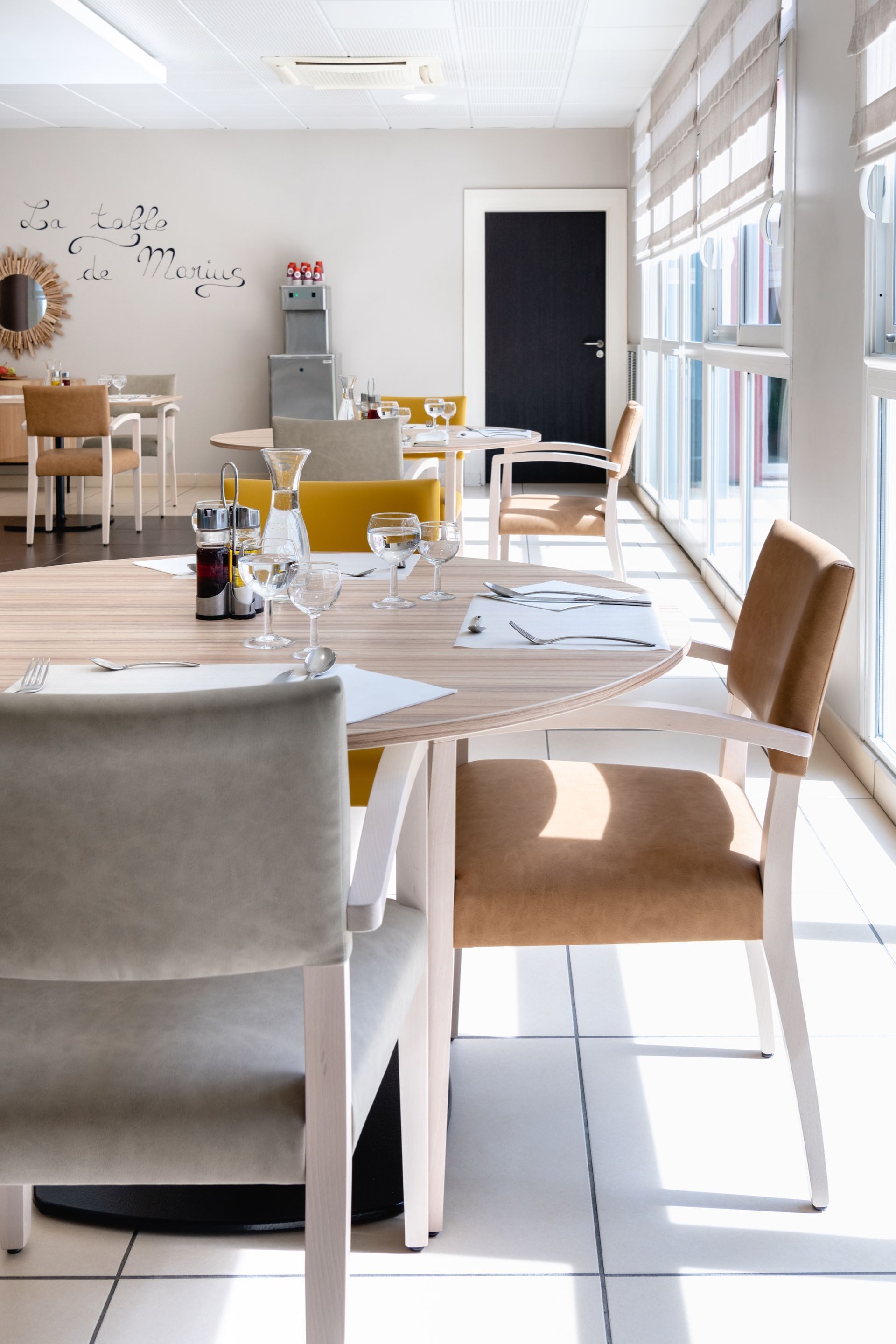 Intérieur de restaurant lumineux avec des tables dressées près d'une grande fenêtre. Chaises beiges et blanches.