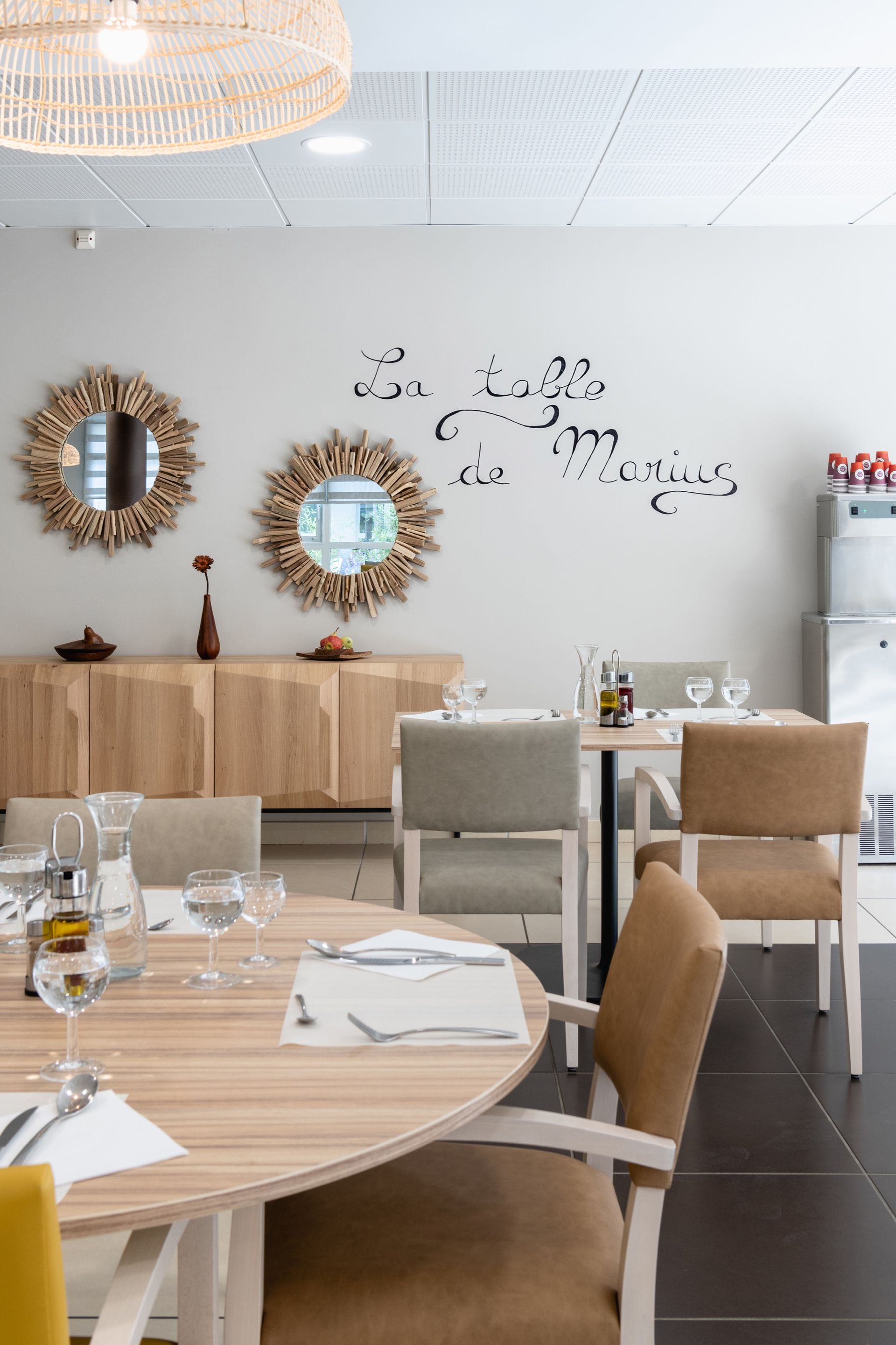 Salle à manger avec table ronde, buffet en bois, miroirs soleil et chaises aux tons neutres.