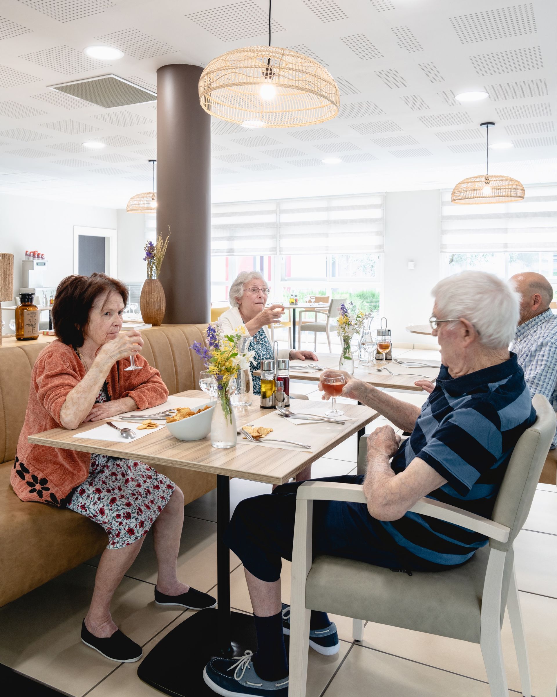 Des gens assis à une table dans une salle à manger lumineuse, conversant et savourant un repas avec des boissons.