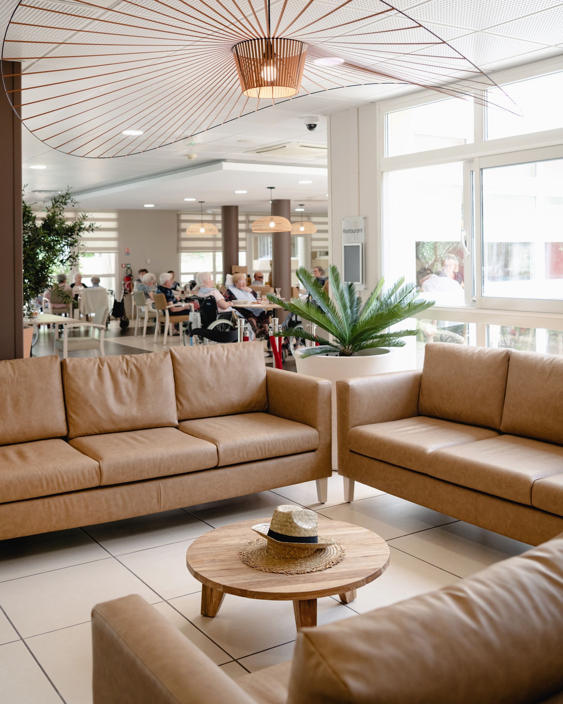 Espace salon avec canapés en cuir, table basse ronde, plante en pot et personnes en arrière-plan.