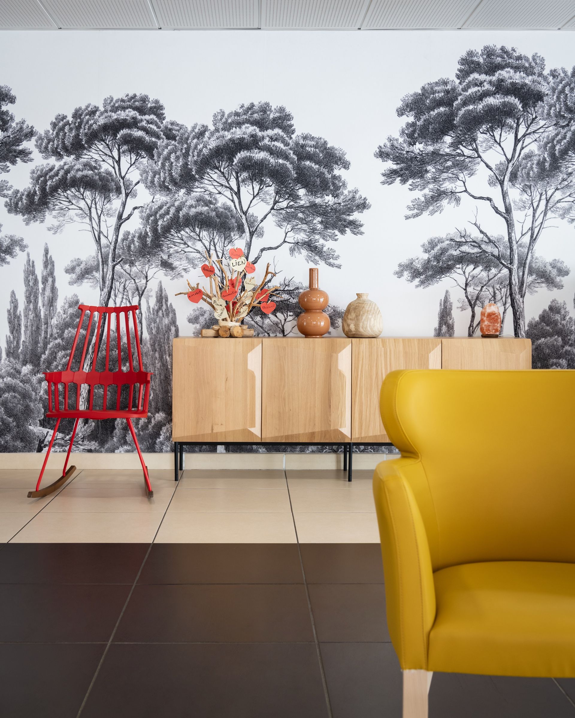 Papier peint forêt noir et blanc avec une armoire en bois, une chaise à bascule rouge et un fauteuil jaune.