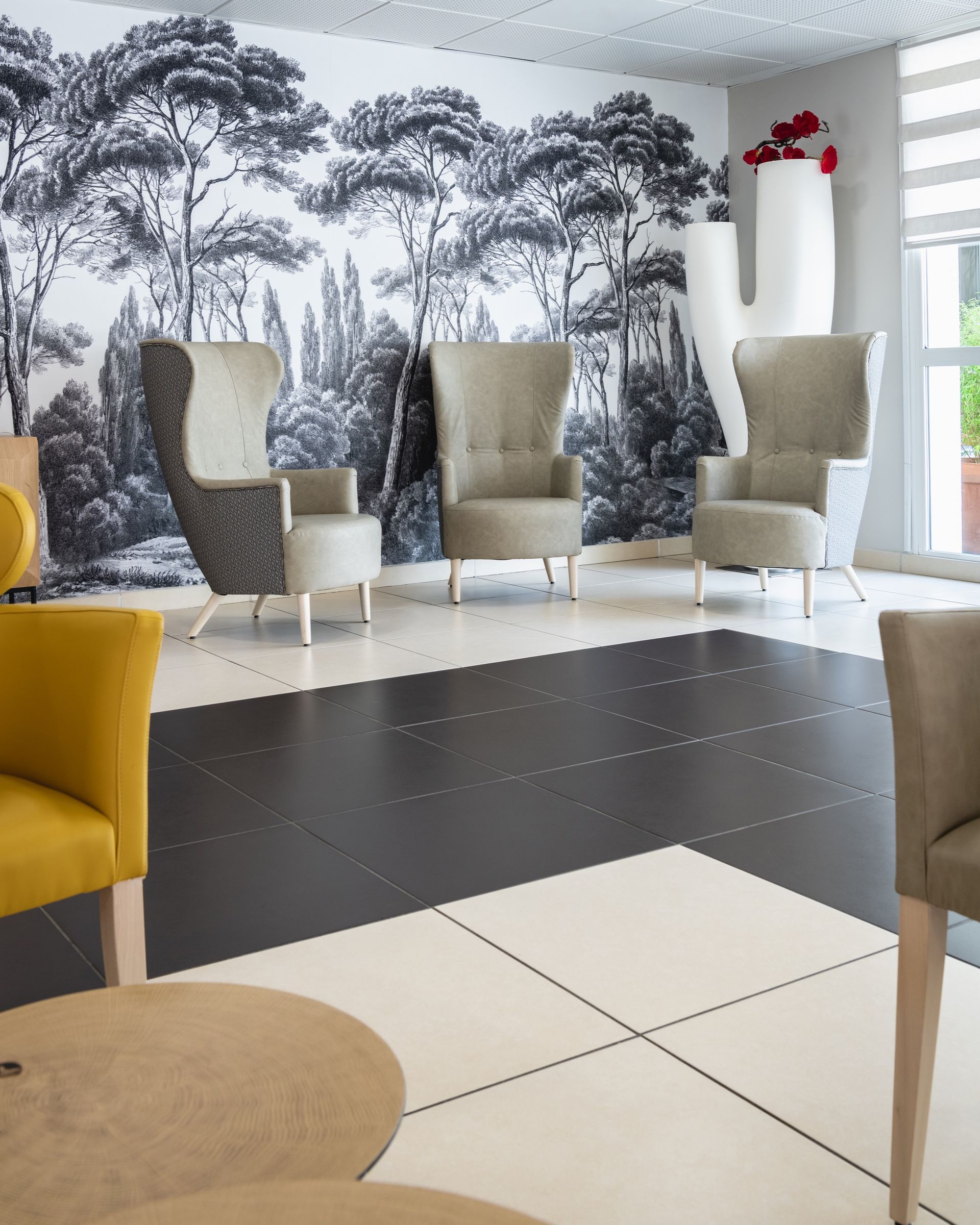 Espace salon avec sol à motifs noir et blanc, fresque paysagère et fauteuils beiges et jaunes.