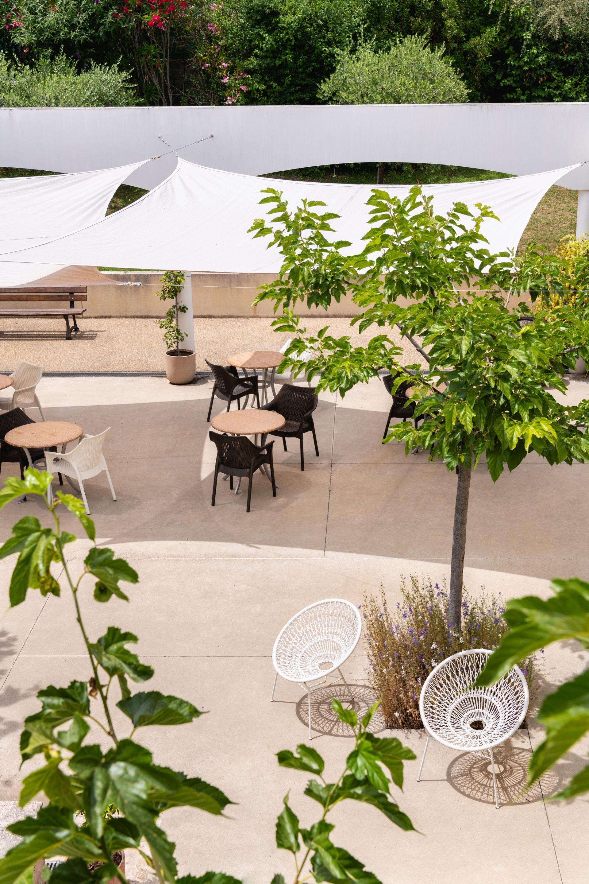 Terrasse extérieure avec tables, chaises et voiles d'ombrage, entourée de verdure.