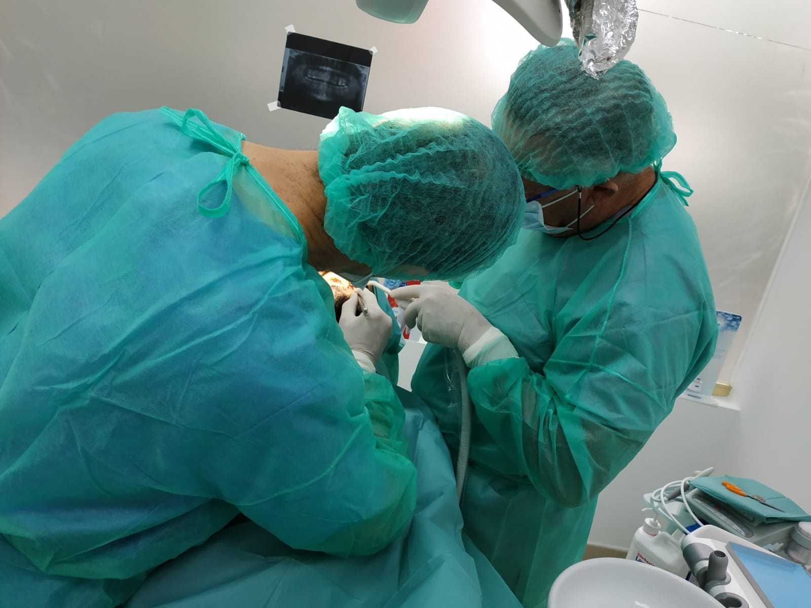 Dos dentistas están trabajando en los dientes de un paciente en un quirófano.