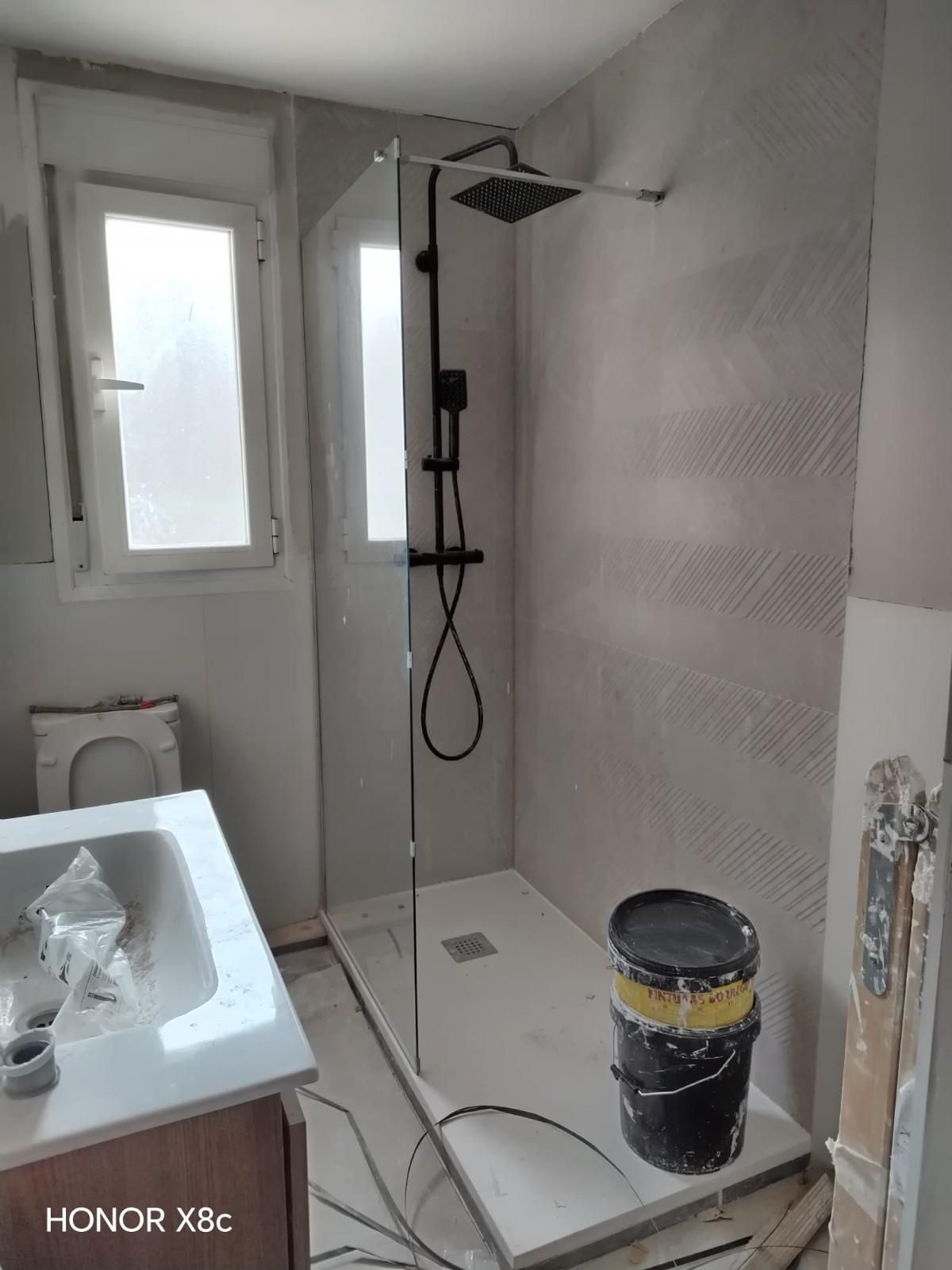 Habitación vacía con suelo de madera clara, paredes blancas, ventana divisoria con marco negro y una escalera a la derecha.