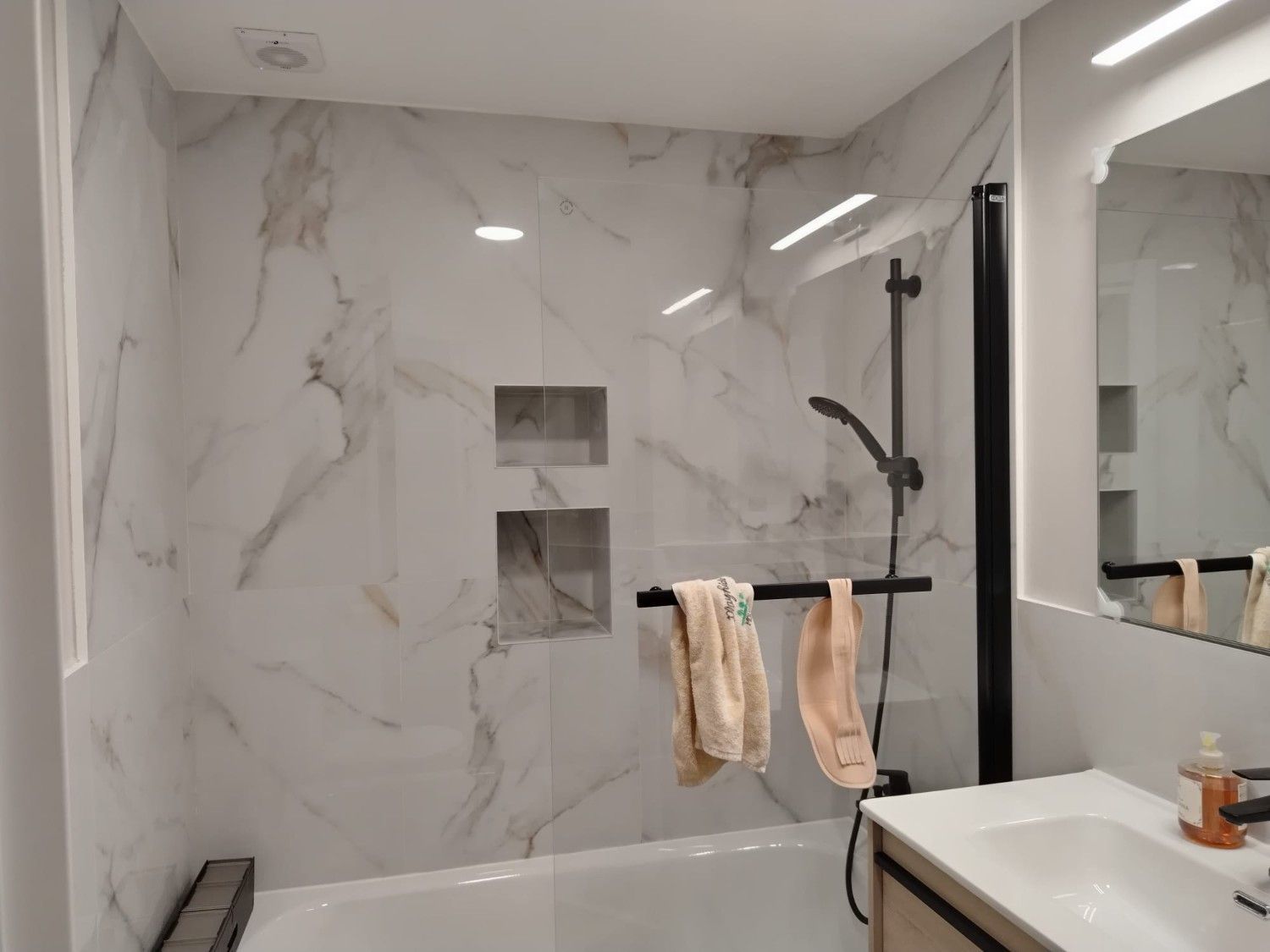 Baño estrecho con ducha, inodoro, lavabo y toallero en un cubículo alicatado.
