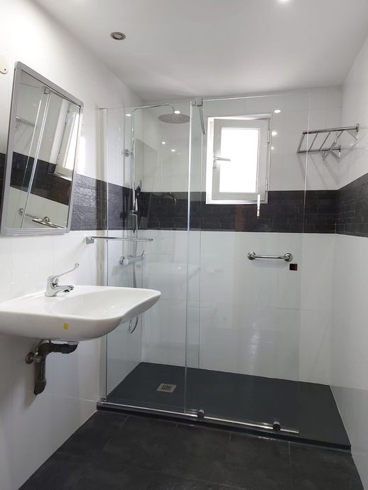 Baño moderno de mármol con ducha de cristal con marco dorado, lavabo sobre encimera y pared con espejo.