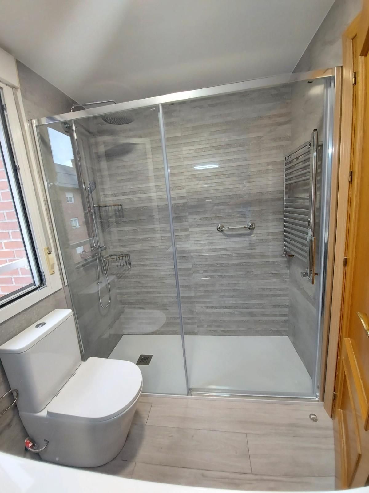 Baño pequeño con ducha de cristal, inodoro, lavabo, espejo de pared y radiador toallero blanco.