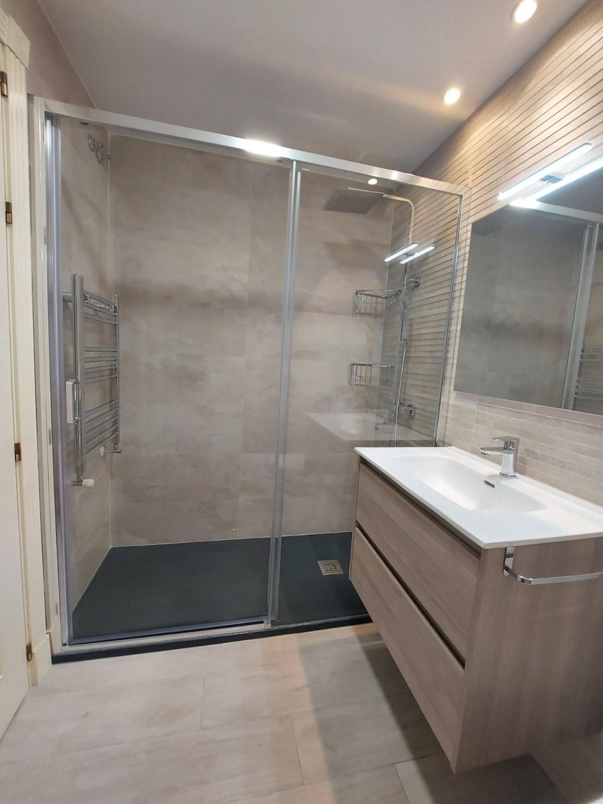 Baño moderno con ducha a ras de suelo de cristal, lavabo con tocador y espejo grande.