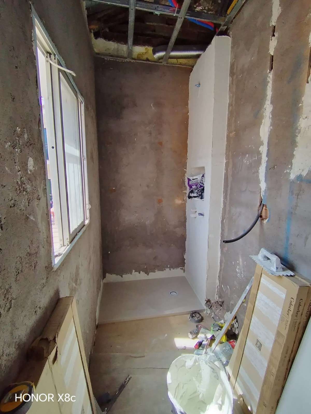 Pasillo estrecho sin terminar, con paredes enlucidas, ventana con luz