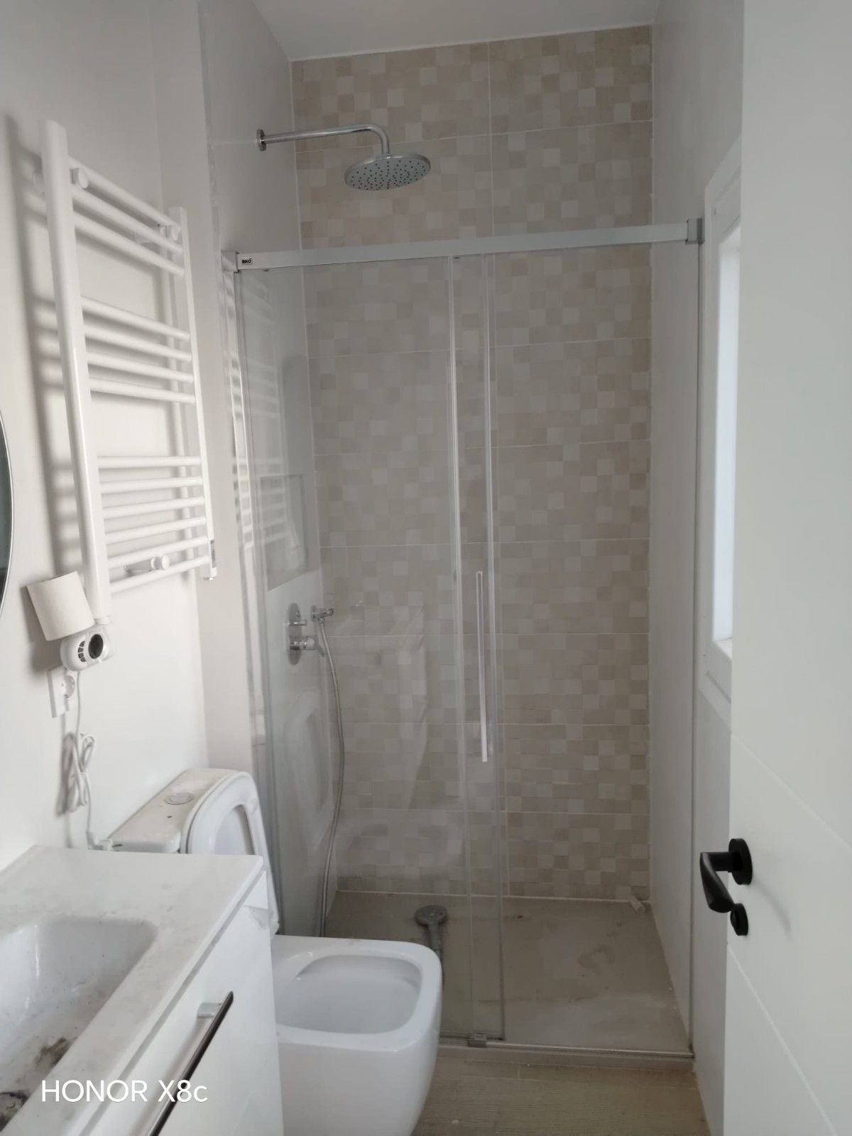 Baño pequeño de color blanco con ducha a ras de suelo, radiador toallero, lavabo e inodoro.