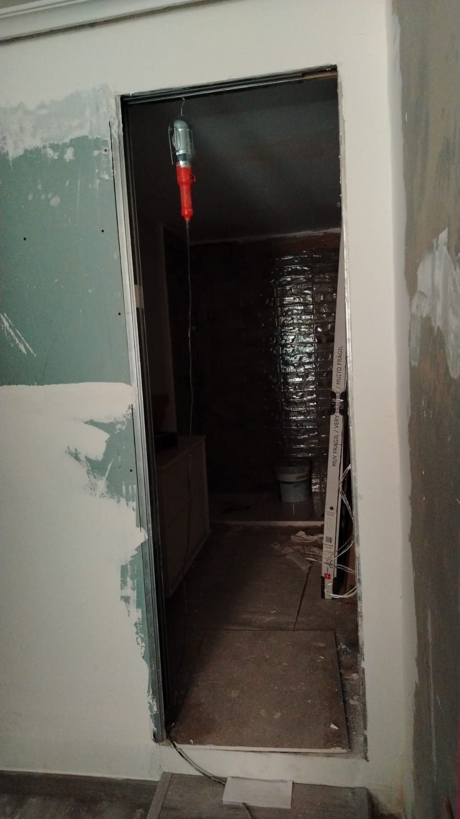Pasillo estrecho sin terminar, con paredes enlucidas, ventana con luz