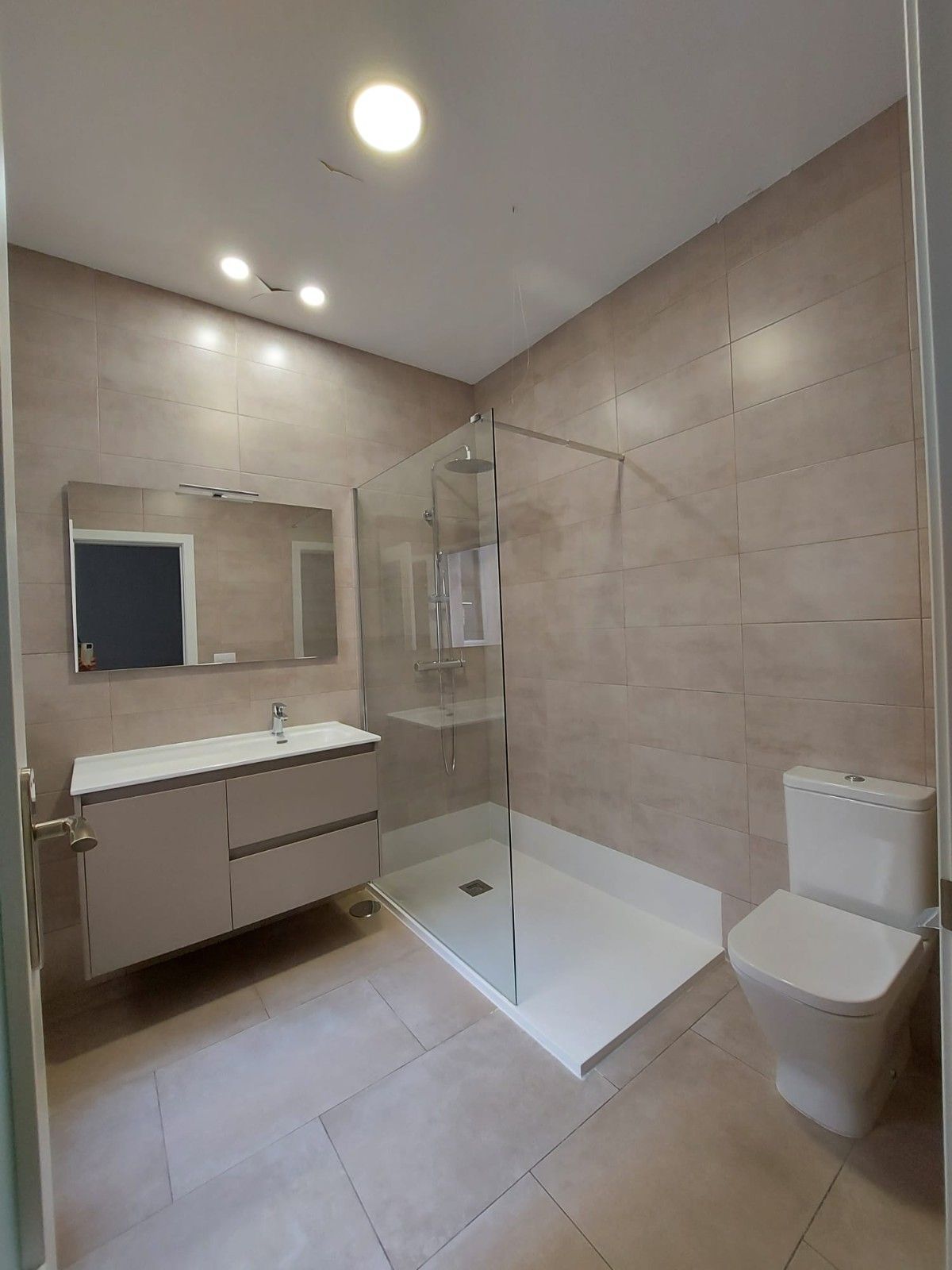 Baño moderno de color beige con tocador, espejo, ducha independiente y inodoro.