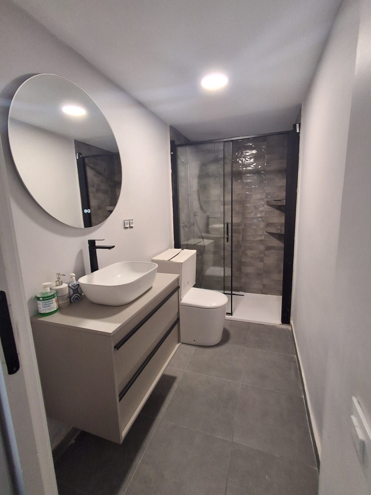Baño estrecho con ducha, inodoro, lavabo y toallero en un cubículo alicatado.