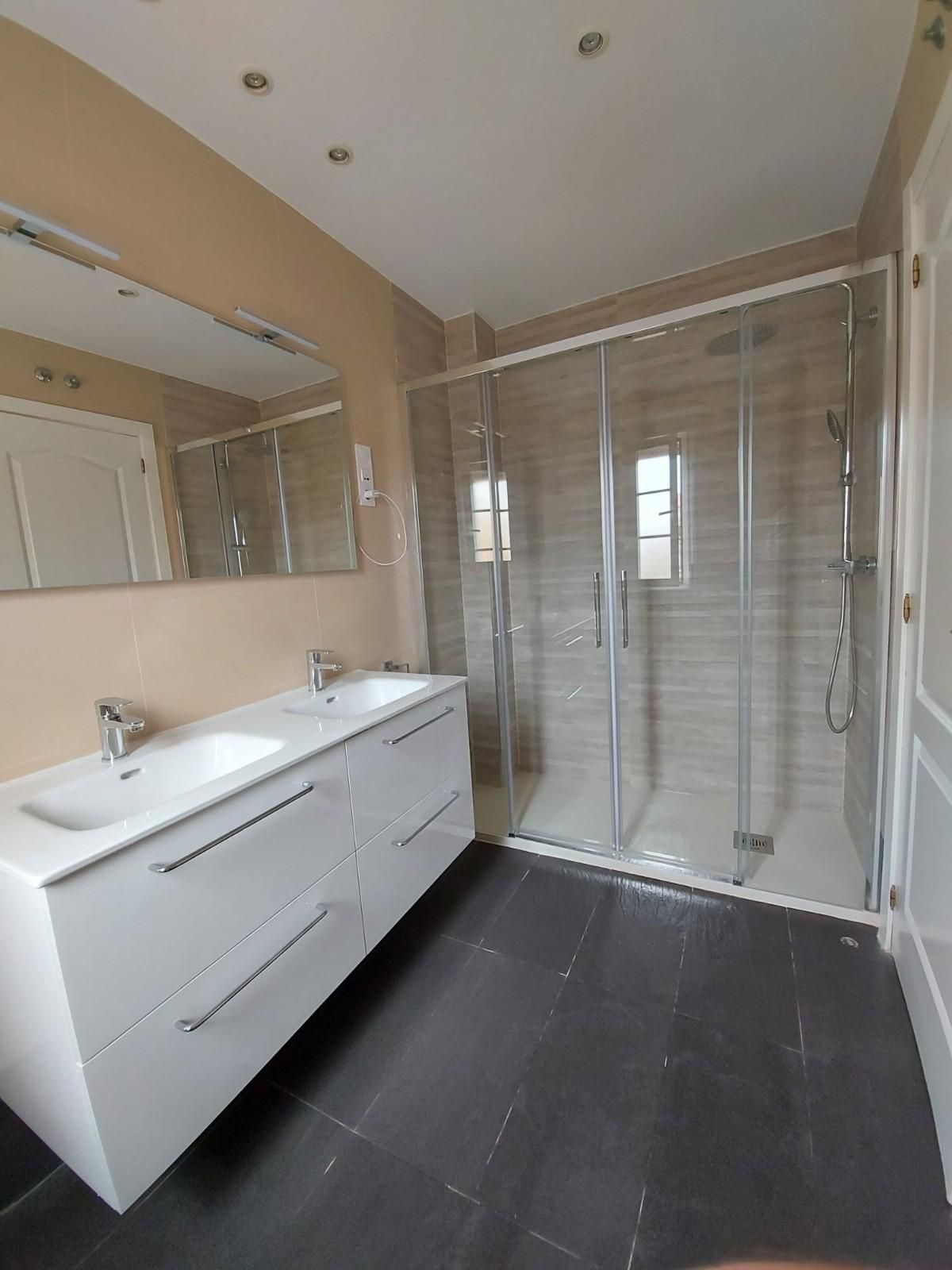 Baño moderno con tocador de doble lavabo, espejo grande y ducha con mampara de cristal.
