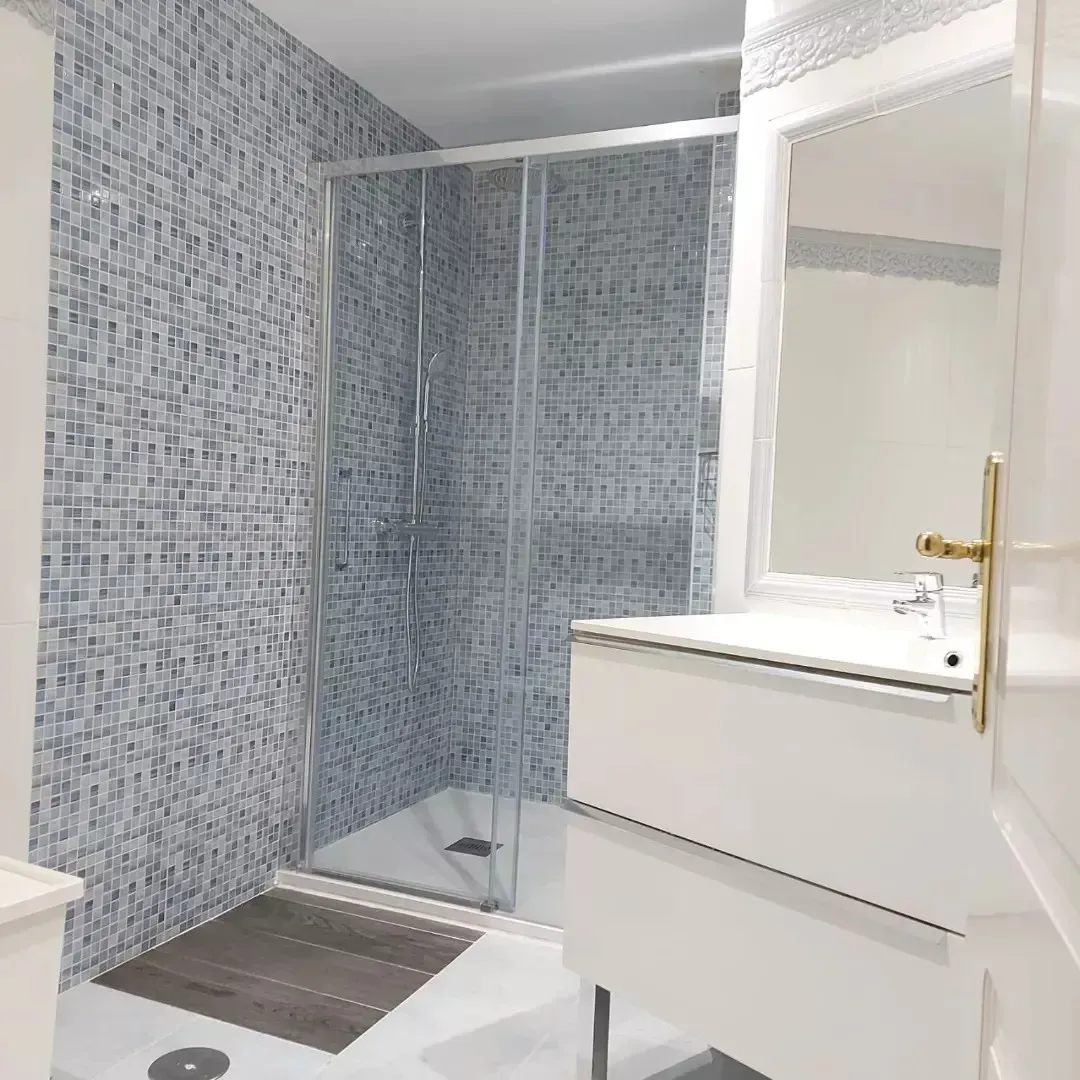 Baño moderno con ducha alicatada, lavabo y grifería blanca.