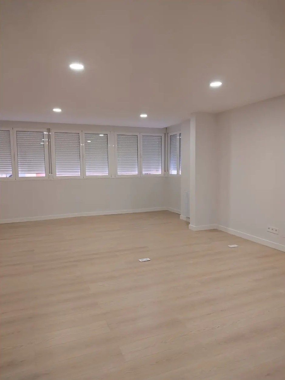 Habitación luminosa y vacía con suelo de madera clara, paredes blancas y ventanas con contraventanas en uno de sus lados.