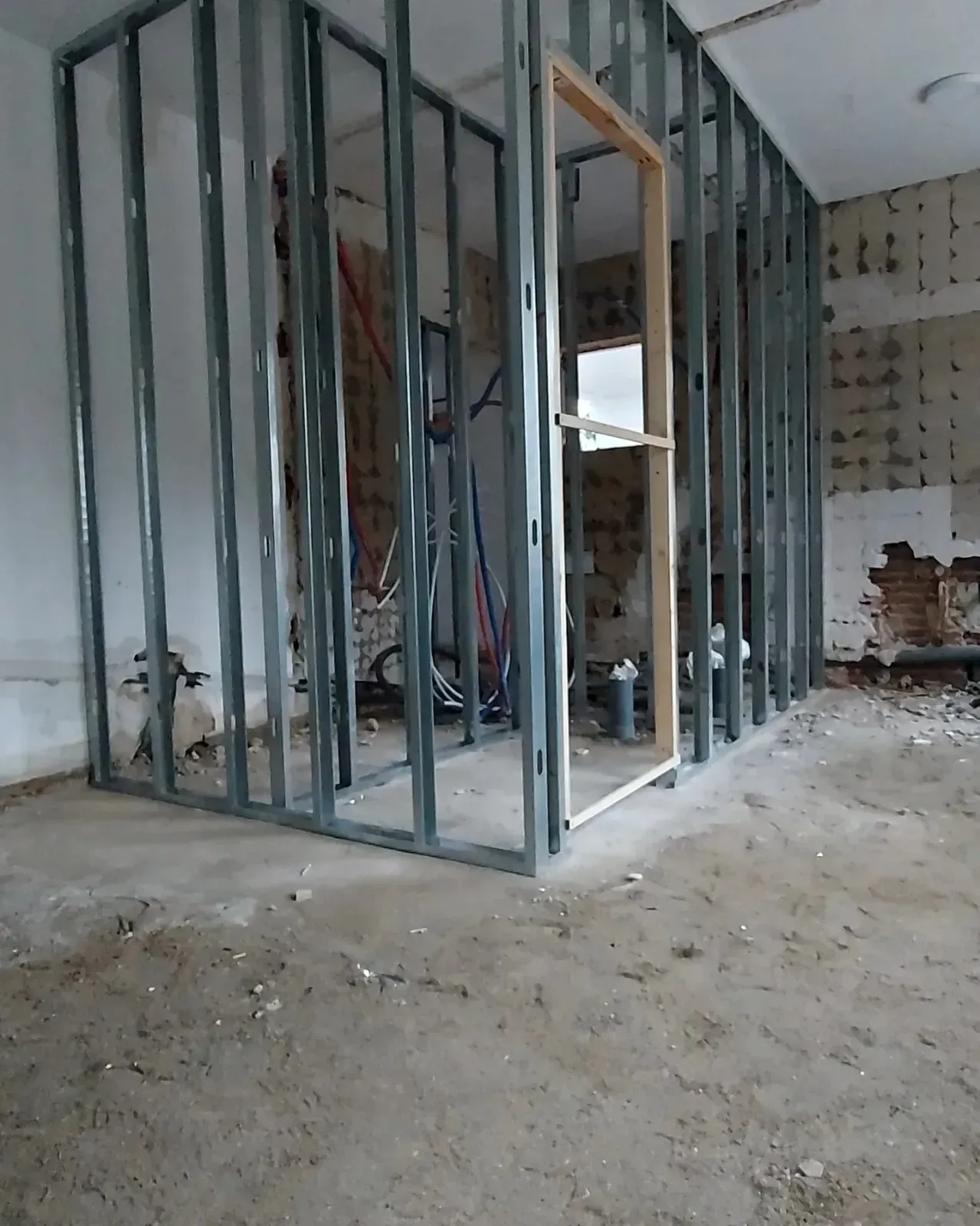 Habitación sin terminar con estructura metálica en las paredes, cableado a la vista y escombros de construcción en el suelo.