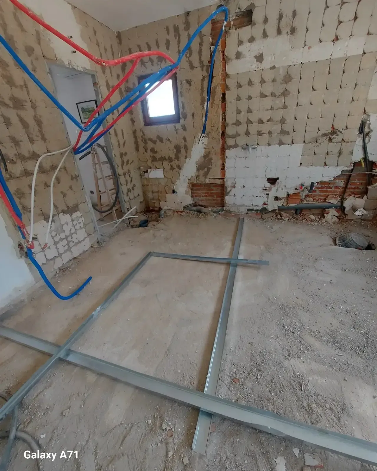 Reforma de una habitación con cableado a la vista, paredes sin terminar, ventana y estructura del suelo sin terminar.