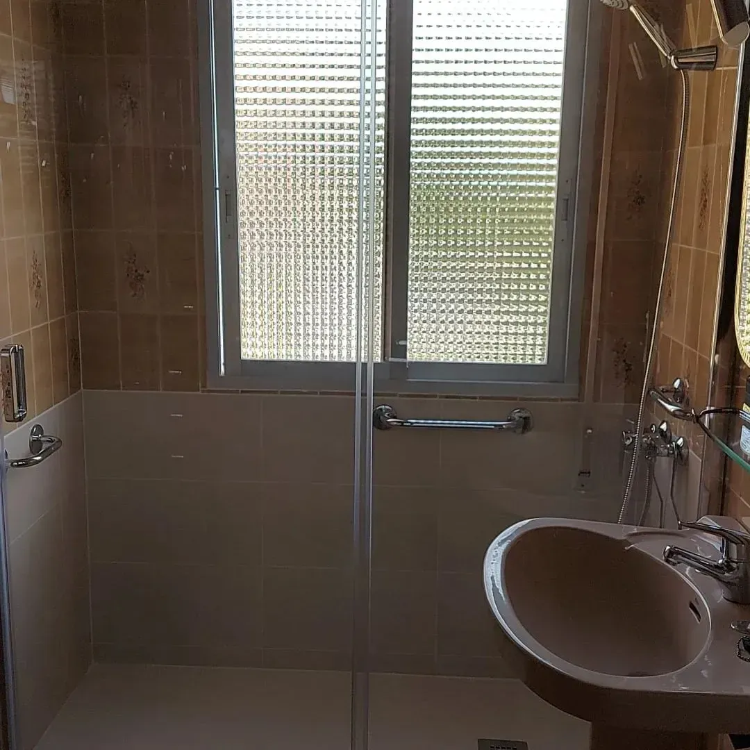 Pequeño baño alicatado con ventana esmerilada, puerta de ducha de cristal y lavabo en primer plano.