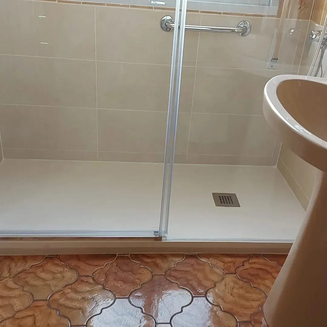 Baño con cabina de ducha alicatada, paredes beige y lavabo en primer plano.