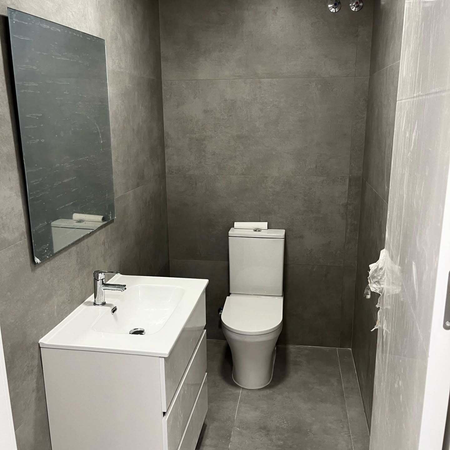 Baño moderno de color gris con lavabo, inodoro y espejo blancos en la pared izquierda.