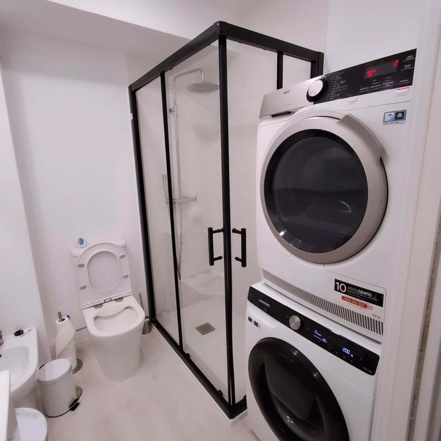 Baño moderno con ducha de cristal, inodoro y lavadora-secadora apilada.