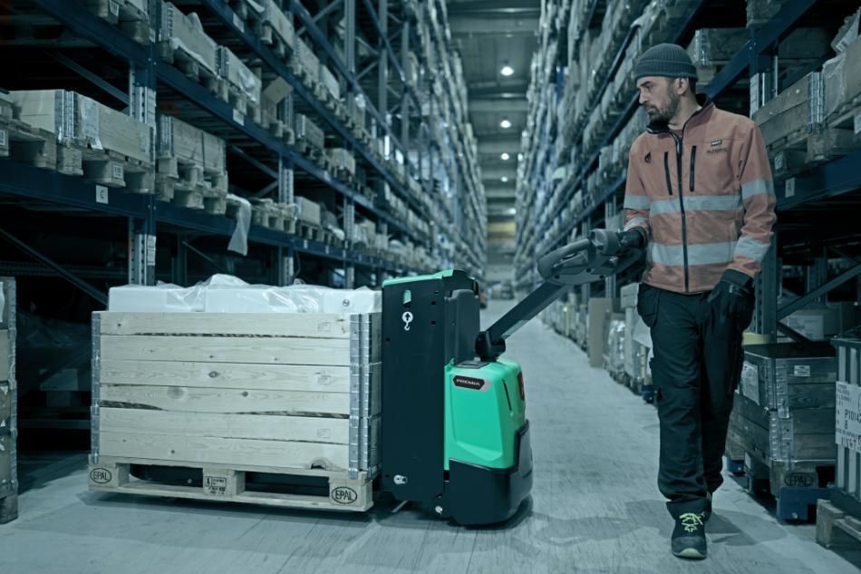 Un employé portant un gilet haute visibilité manœuvre un transpalette électrique vert pour déplacer des marchandises dans une allée d'entrepôt.