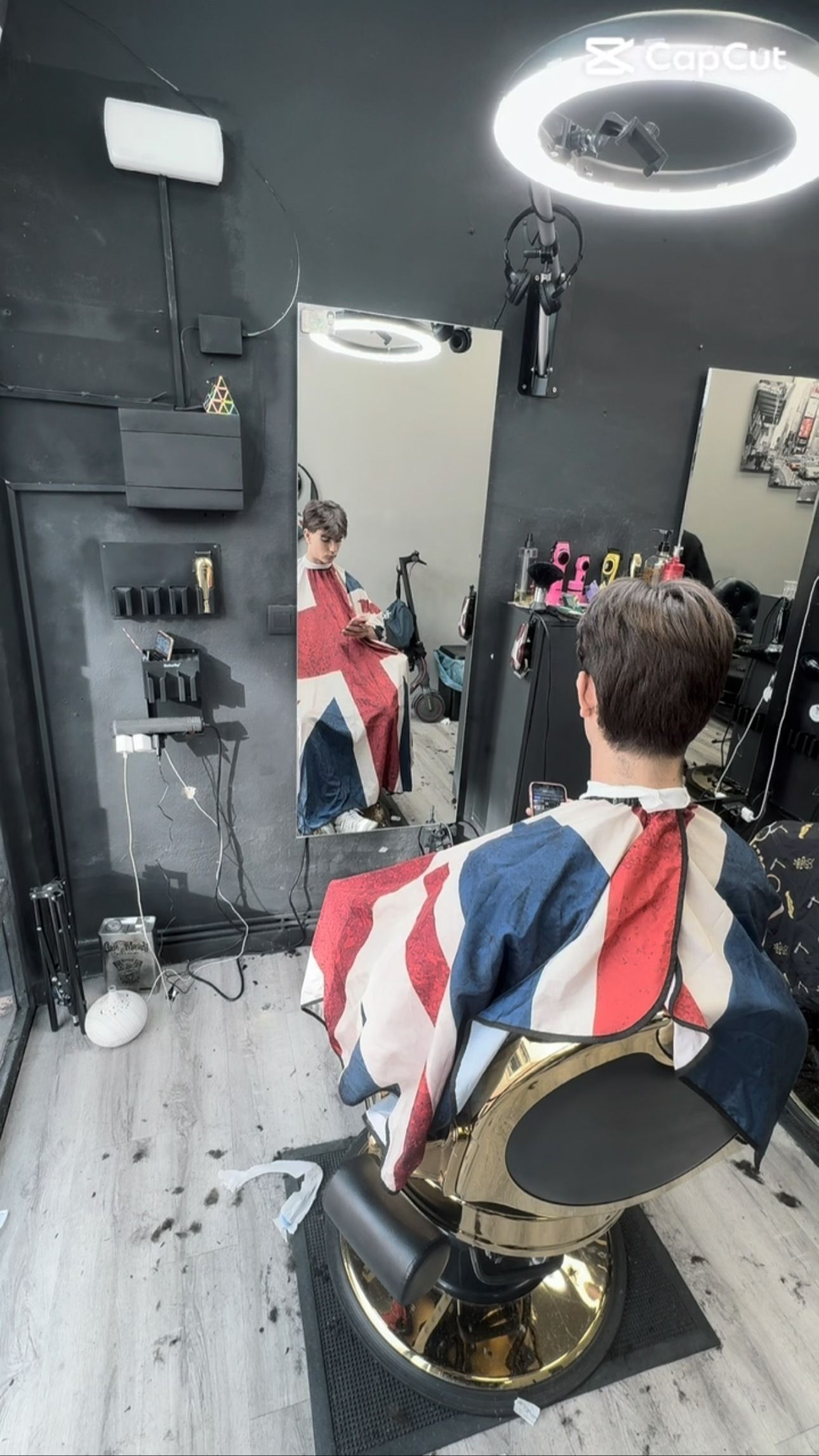 Persona cortándose el pelo en una barbería, reflejada en un espejo. Lleva una capa de barbero con el diseño de la Union Jack.