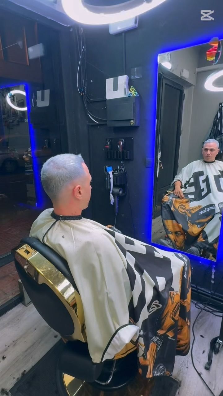 Hombre con cabello plateado cortándose el pelo en una barbería, mirándose en el espejo.