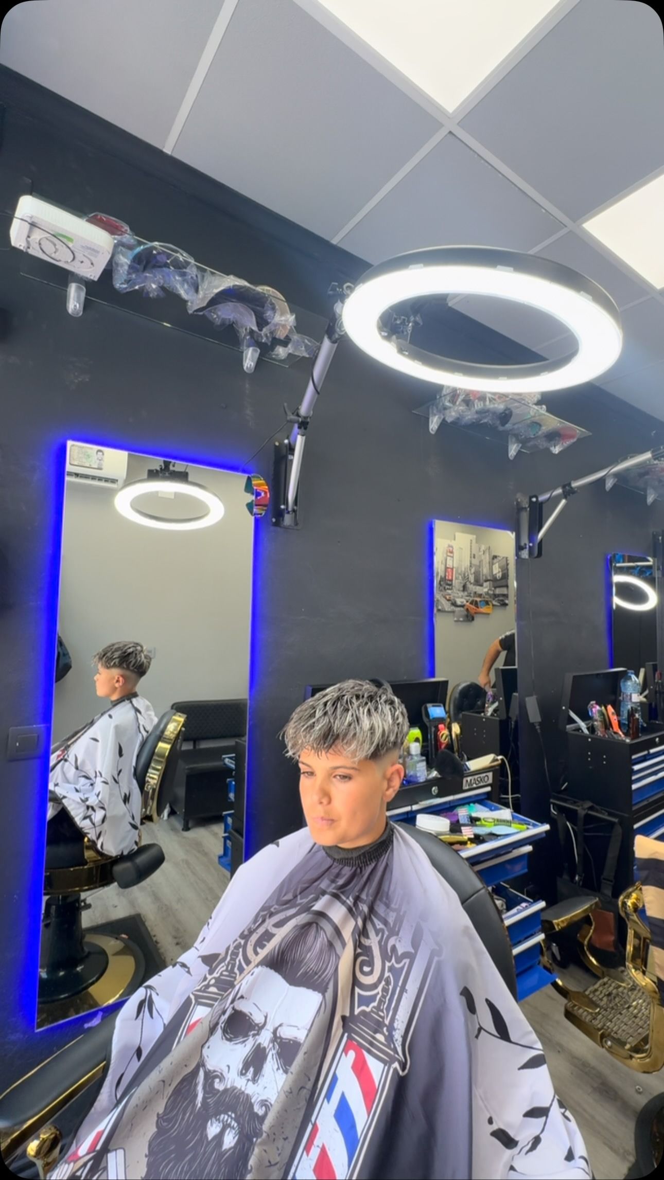 Persona cortándose el pelo en una barbería con un anillo de luz y vistiendo una capa estampada.