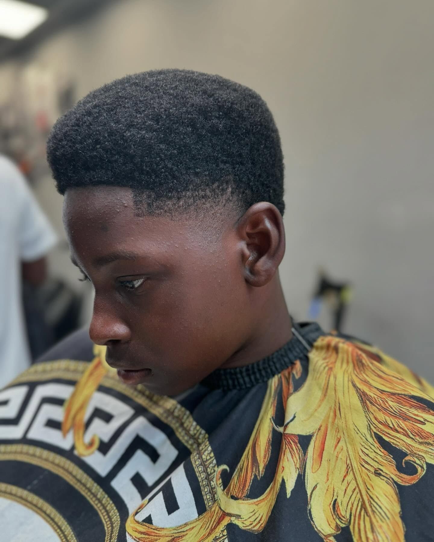 Niño con un corte de pelo bajo y cabello negro rizado, vistiendo una capa de salón.