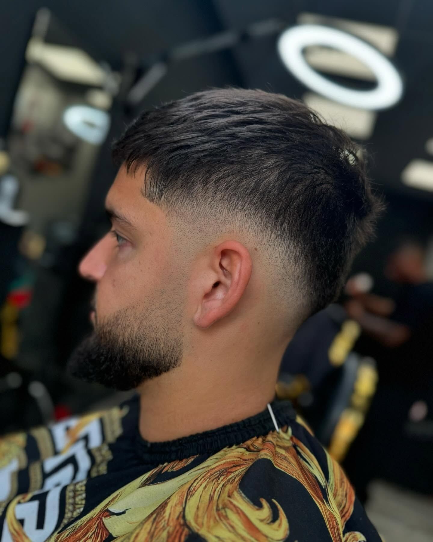 Hombre con un corte de pelo descolorido y barba recortada, en un entorno de barbería.