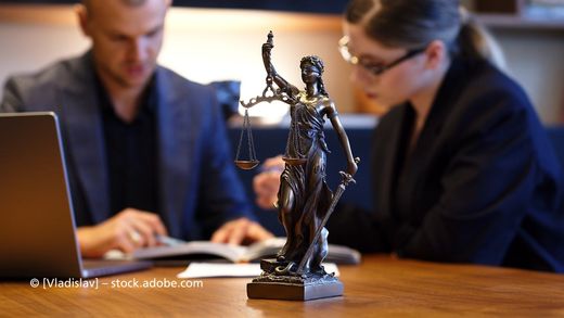 Anwaltskanzlei Kay Schnarrer, Figur Justitia, im Hintergrund Mann und Frau vor Laptop